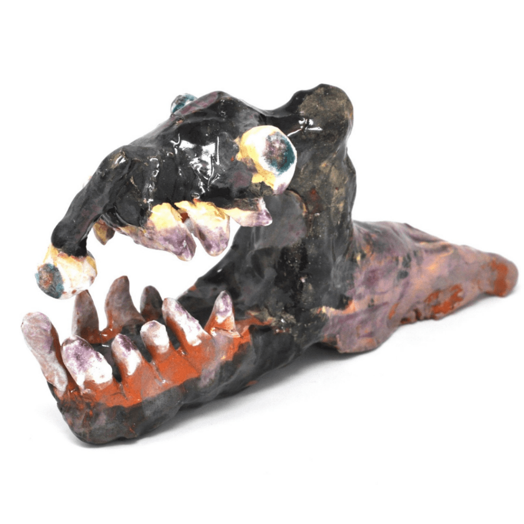 A ceramic piece with a slimy glaze of a gruesome figure with a reptilian head, a slug-like body, a lidless eye, and a jaw full of jagged teeth. One tooth has an eyeball growing from it. 