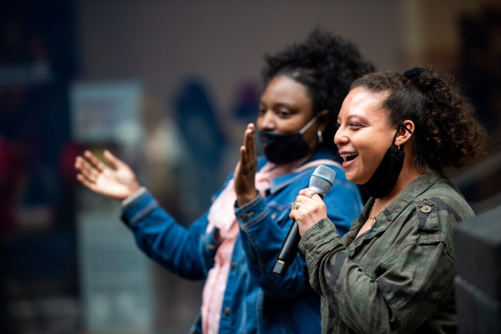 Two NIAD artists, Shawna clapping on the left and Esme with the microphone on the right, attend SFMOMA mini murals