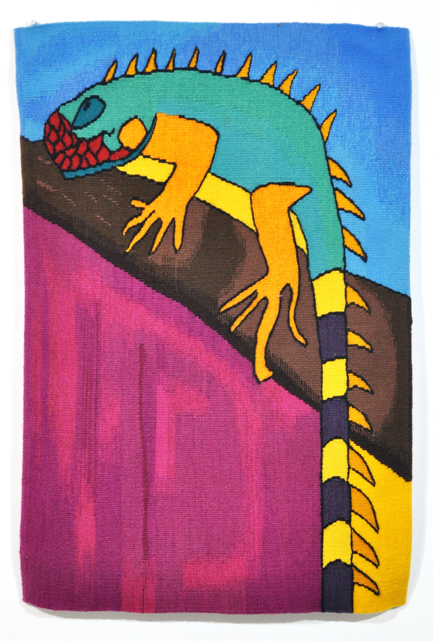 a brightly colored tapestry of an iguana - blue, orange, yellow and black -resting on a branch